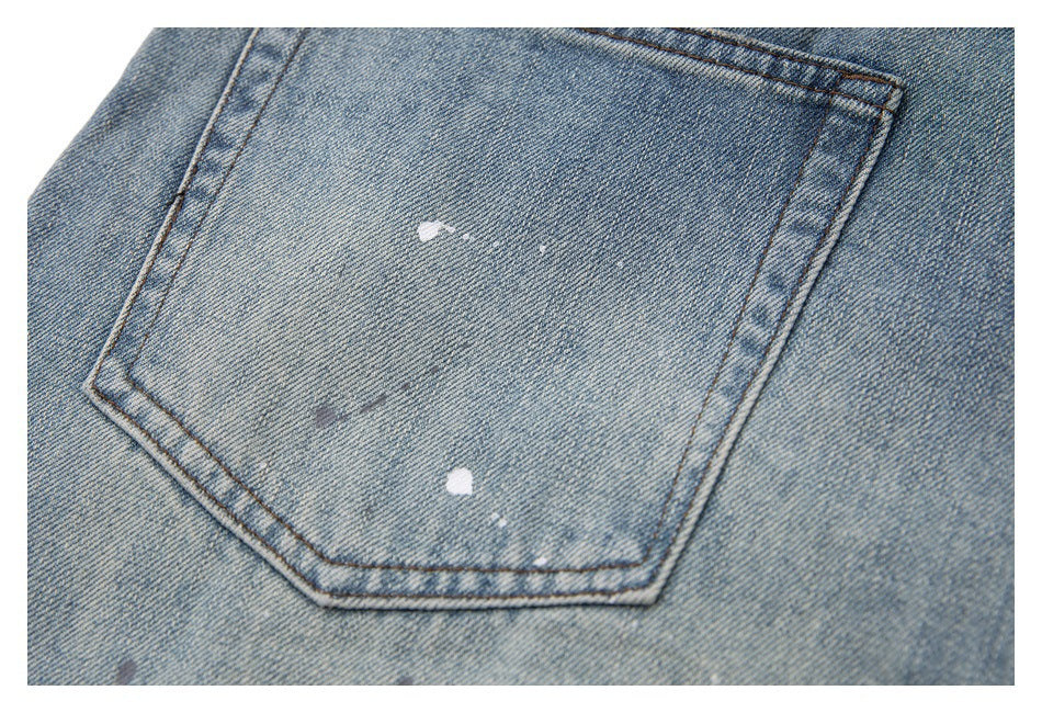 Close-up of a light blue denim back pocket with white paint-like marks and contrast stitching.