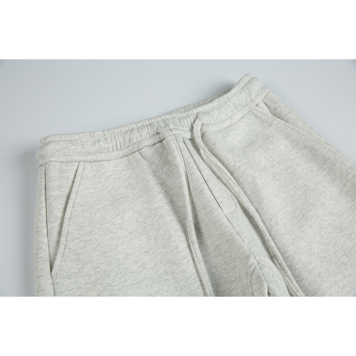 Close-up of light gray marl sweatpants showing the elastic drawstring waistband and angled front pockets.