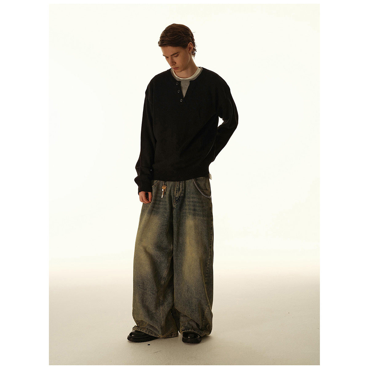 Man wearing a black button-placket knit sweater over a light shirt with very wide washed jeans.