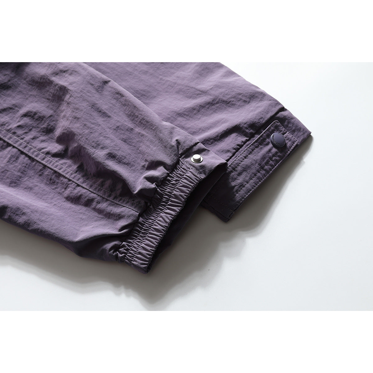 Close-up of a plum jacket sleeve cuff with elastic gathering and an adjustable snap tab.