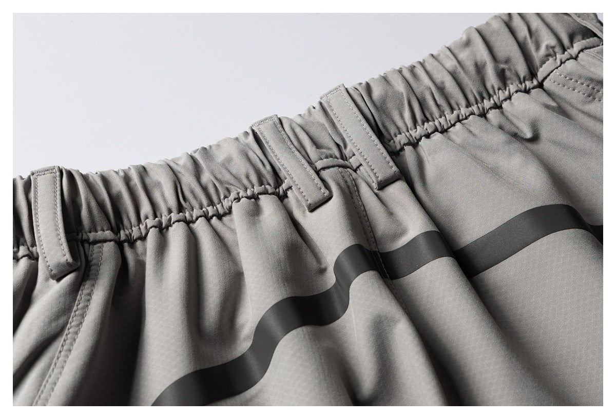 Close-up of gray trousers with an elastic waistband, belt loops, and a black wavy stripe.