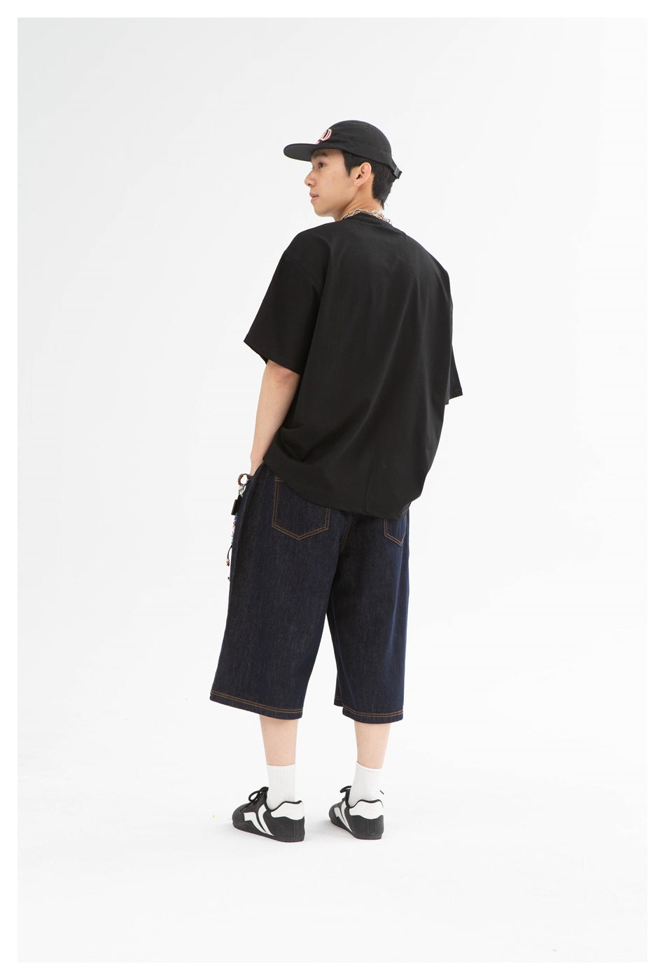 Back view of model wearing dark indigo knee-length denim shorts with back patch pockets and a black T-shirt