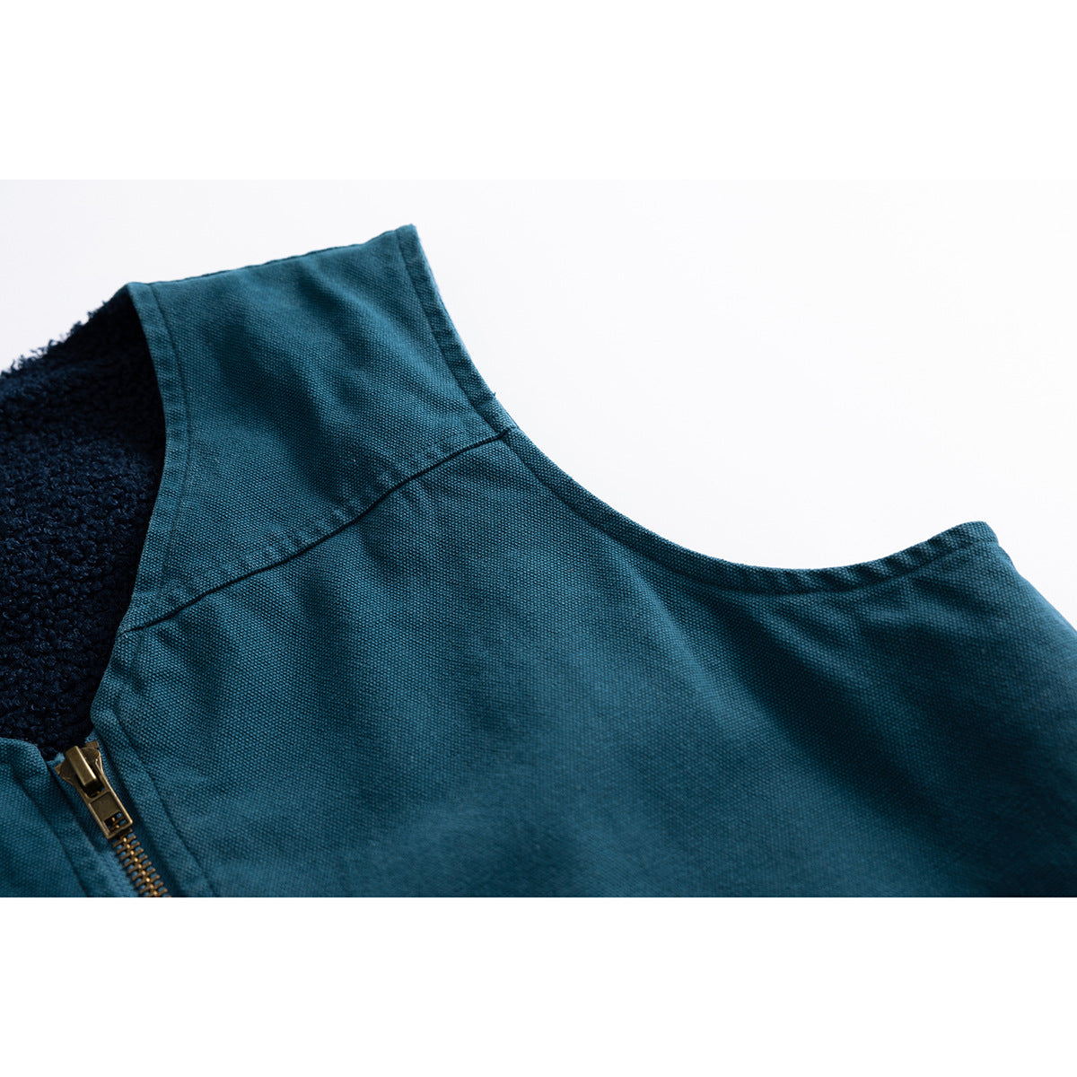 Close-up of the teal vest's shoulder seam and armhole, with dark lining and part of the brass-tone zipper visible.
