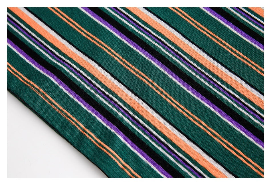 Close-up of dark green knit fabric with repeating orange, purple, black and white stripes.