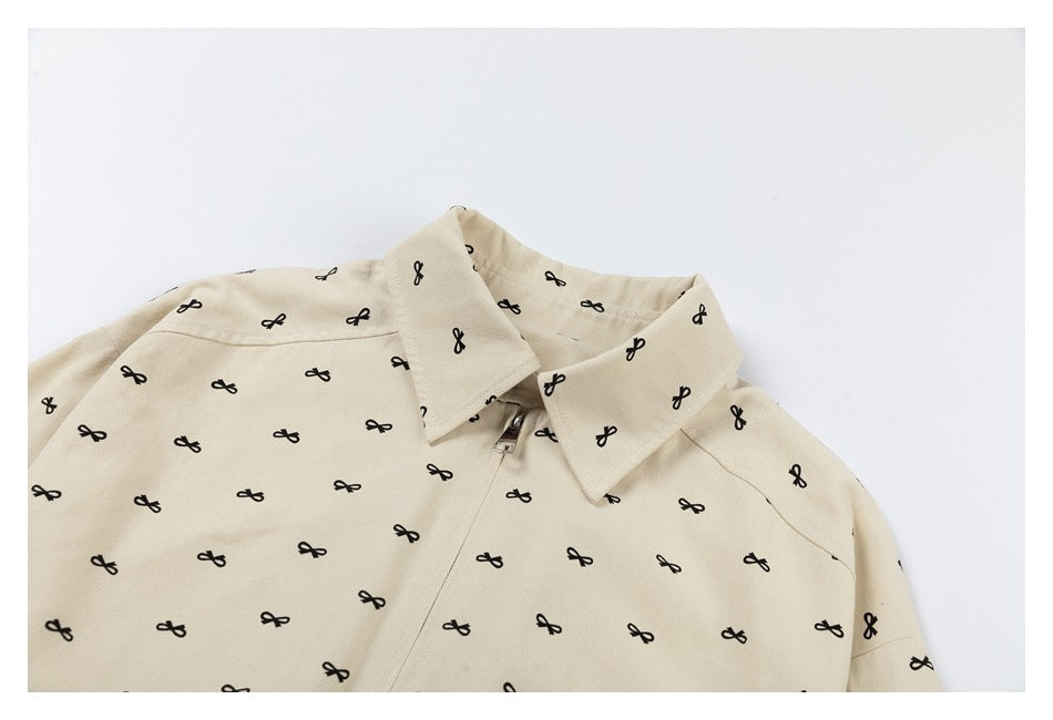 Close-up of the cream jacket's pointed collar, upper shoulders and partially visible zipper, with black bow motifs.