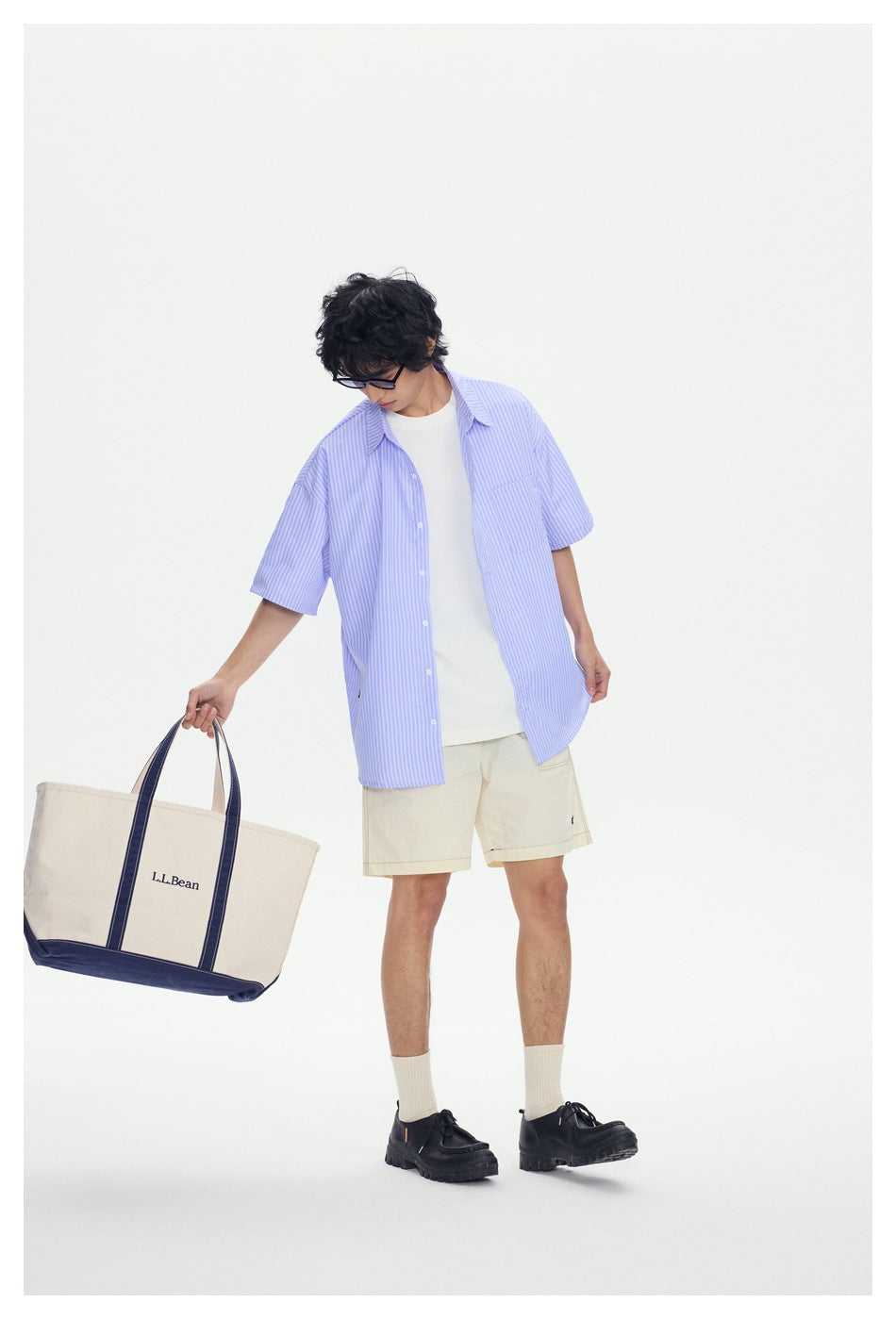 Model wearing an oversized light blue-and-white striped short-sleeve shirt over a white tee, with cream shorts.