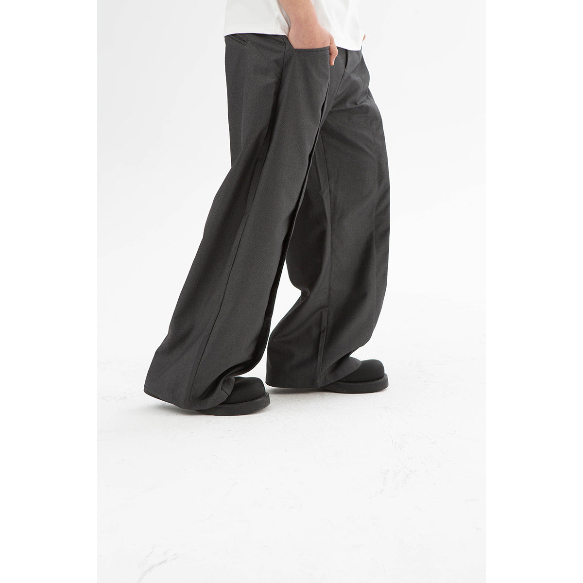 Close view of loose charcoal-gray trousers worn with a white shirt, showing the wide legs and side pocket.