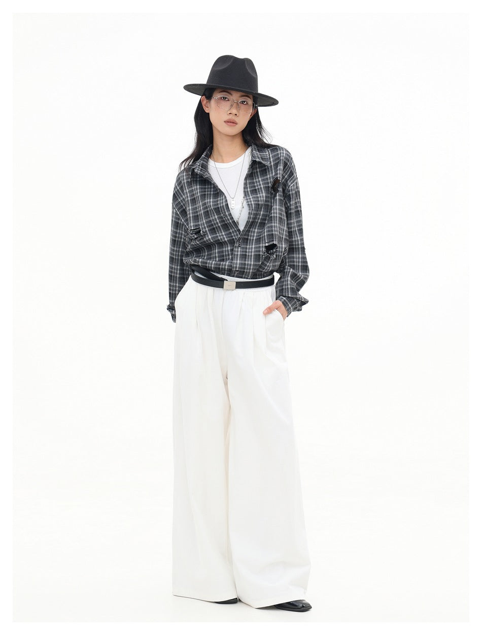 Full-length model wearing a charcoal gray plaid shirt tucked into wide white trousers, with a black hat and belt.