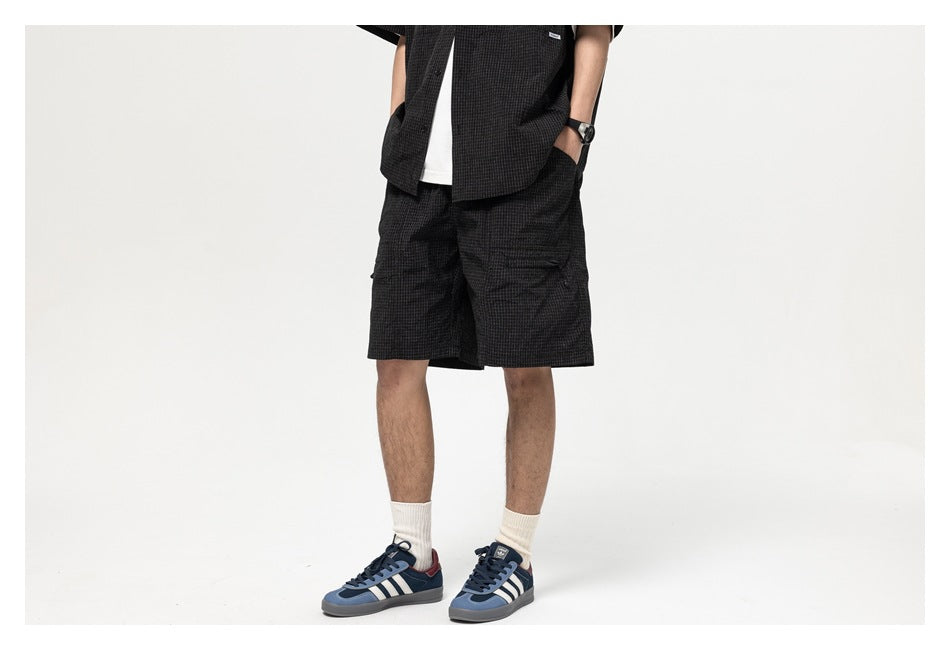 Front view of a person wearing black check shorts with a matching shirt, white socks, and blue sneakers.