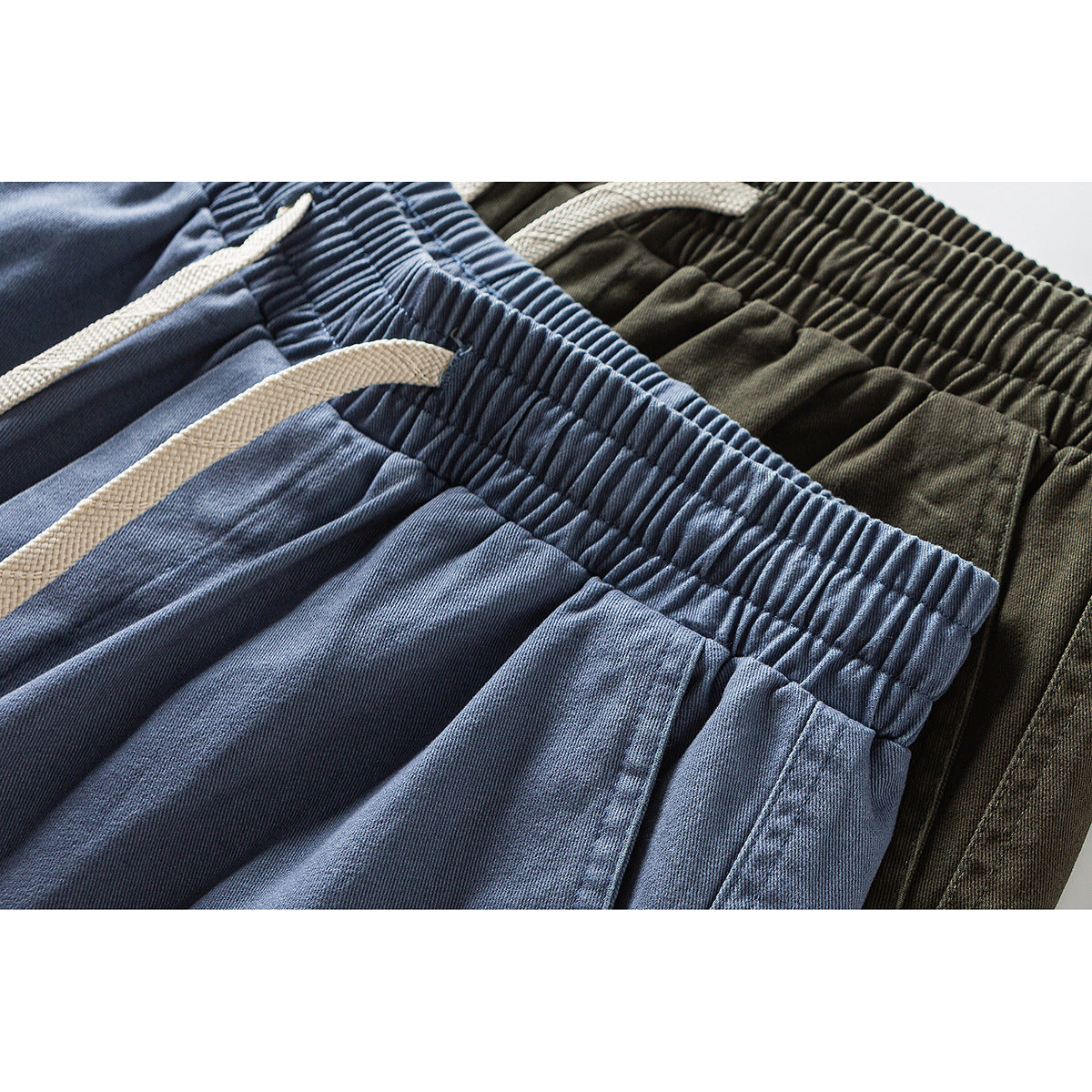 Close-up of gathered waistbands and white drawstrings on blue and olive cargo pants.