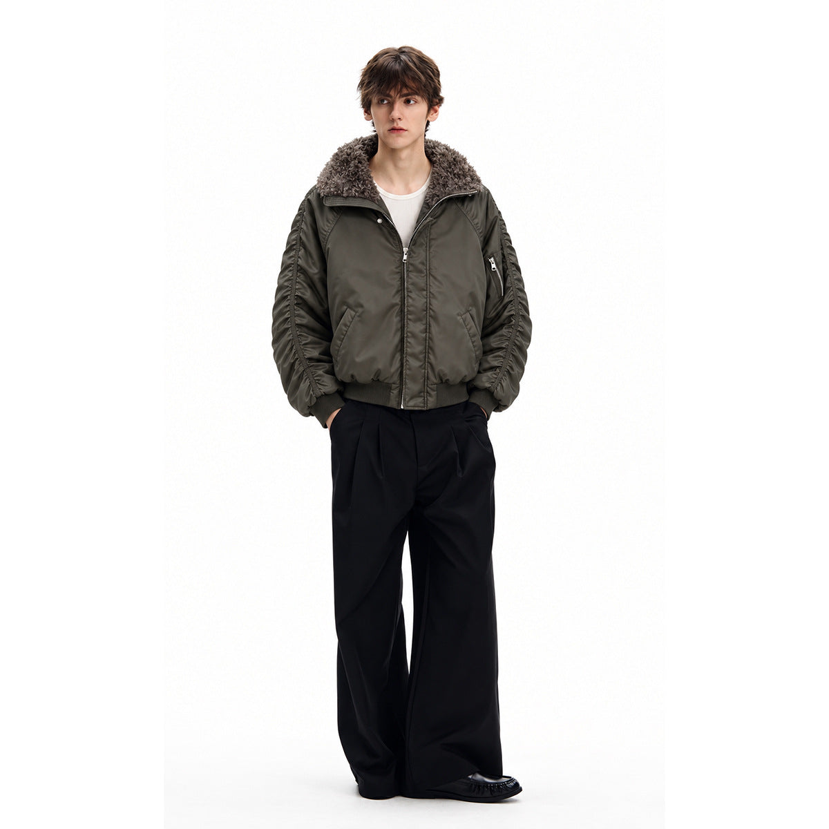 Full-length male model wearing a dark olive bomber jacket with a plush gray collar and black wide-leg trousers.