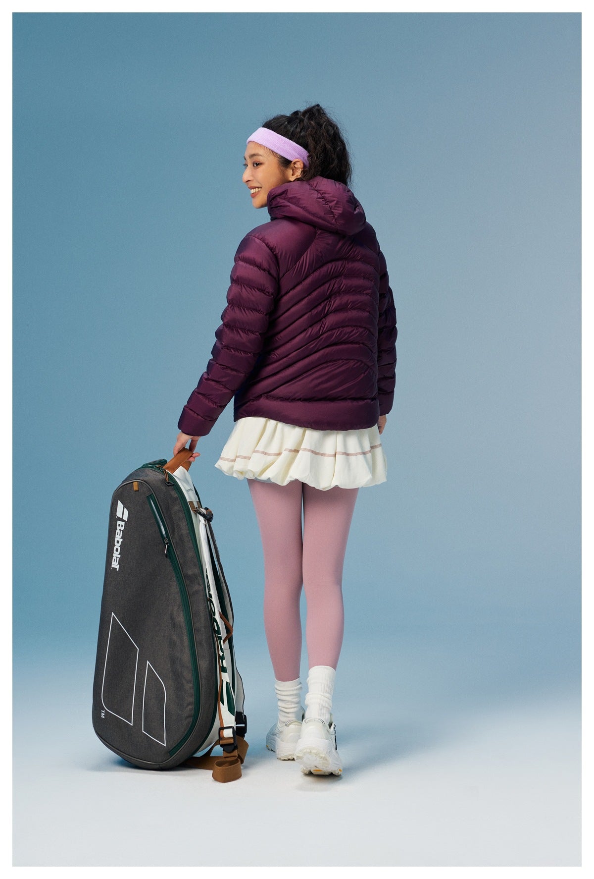 Rear view of a model wearing a plum quilted hooded jacket with diagonal back stitching and pink leggings.
