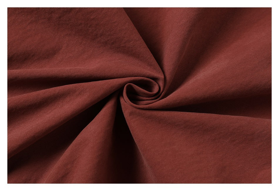 Close-up of rust-brown fabric gathered into folds, showing its fine surface texture.