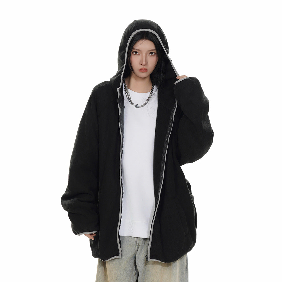 Model wearing an open oversized black hooded zip jacket with light trim over a white top and loose light-wash jeans.