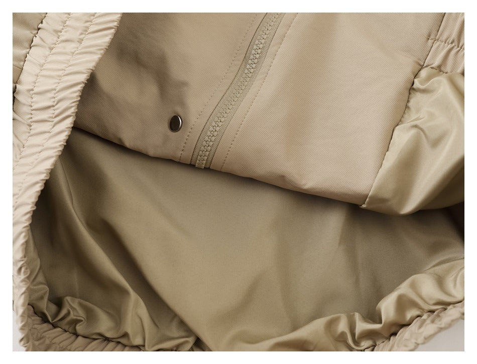 Close-up of a beige garment showing a zipper, snap fastener, and gathered fabric edges.