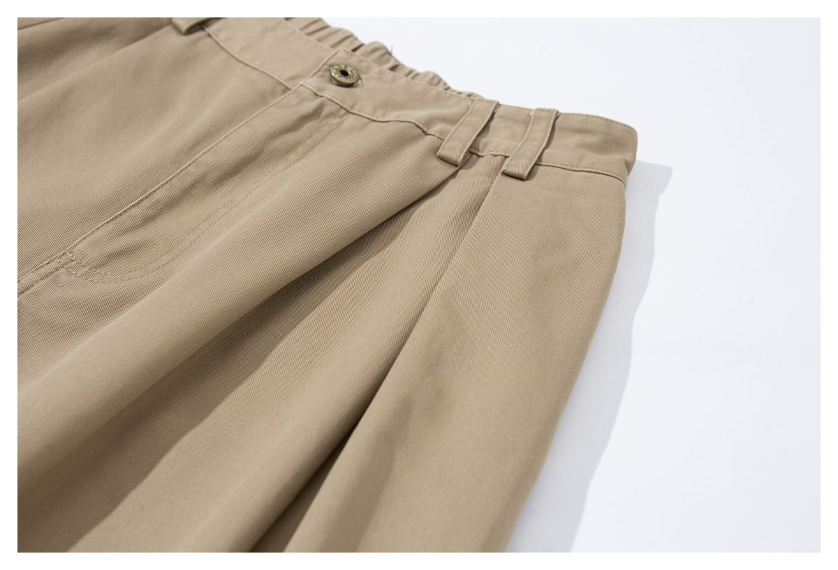 Close-up of tan trousers showing the buttoned waistband, belt loops, front pleats and pocket opening.