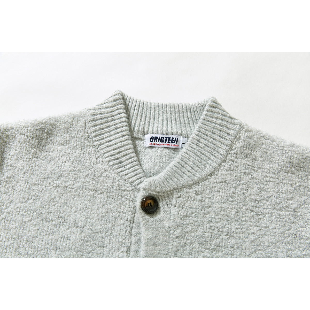 Close-up of a light gray cardigan's ribbed shawl collar, button, textured knit, and sewn neck label.