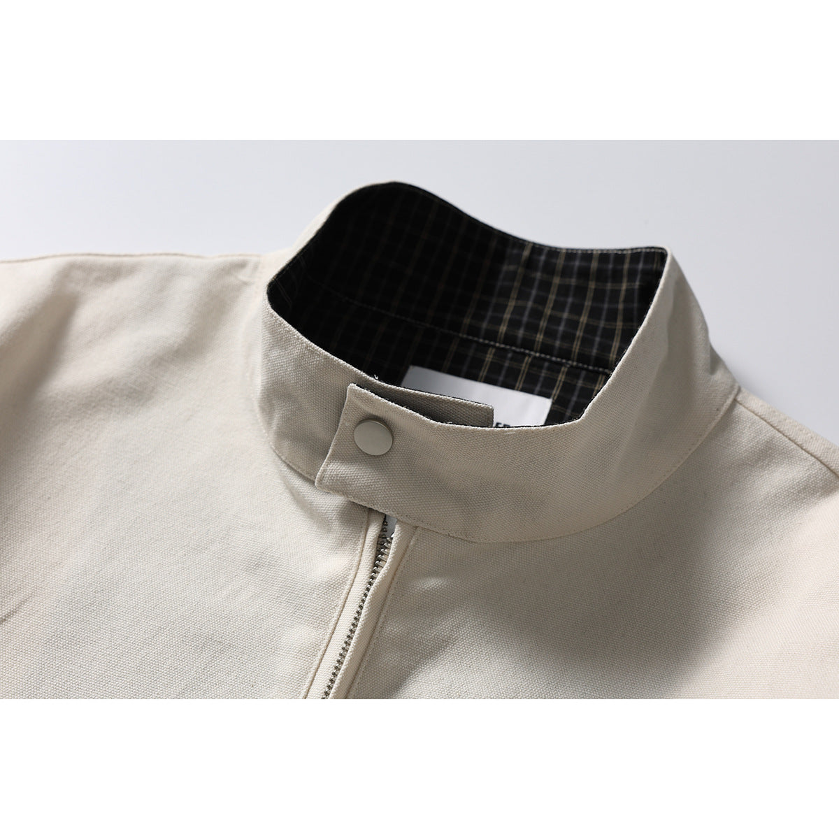 Close-up of an ivory jacket's stand collar, snap tab, zipper, and dark plaid inner lining.