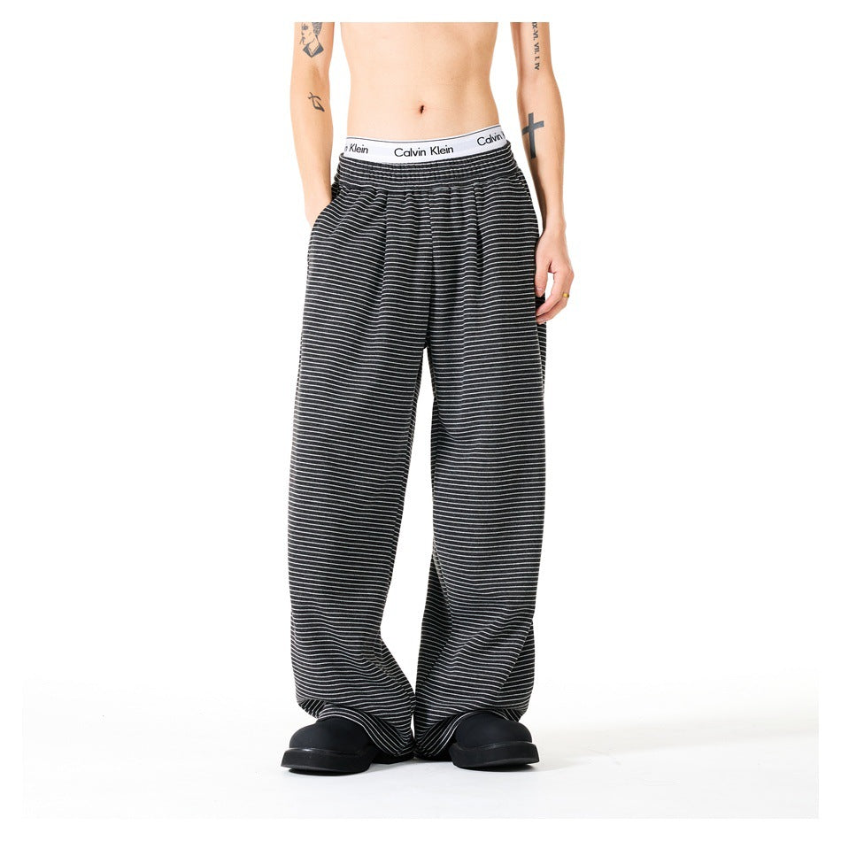 Front view of a model wearing loose black trousers with thin white stripes and a white branded waistband.