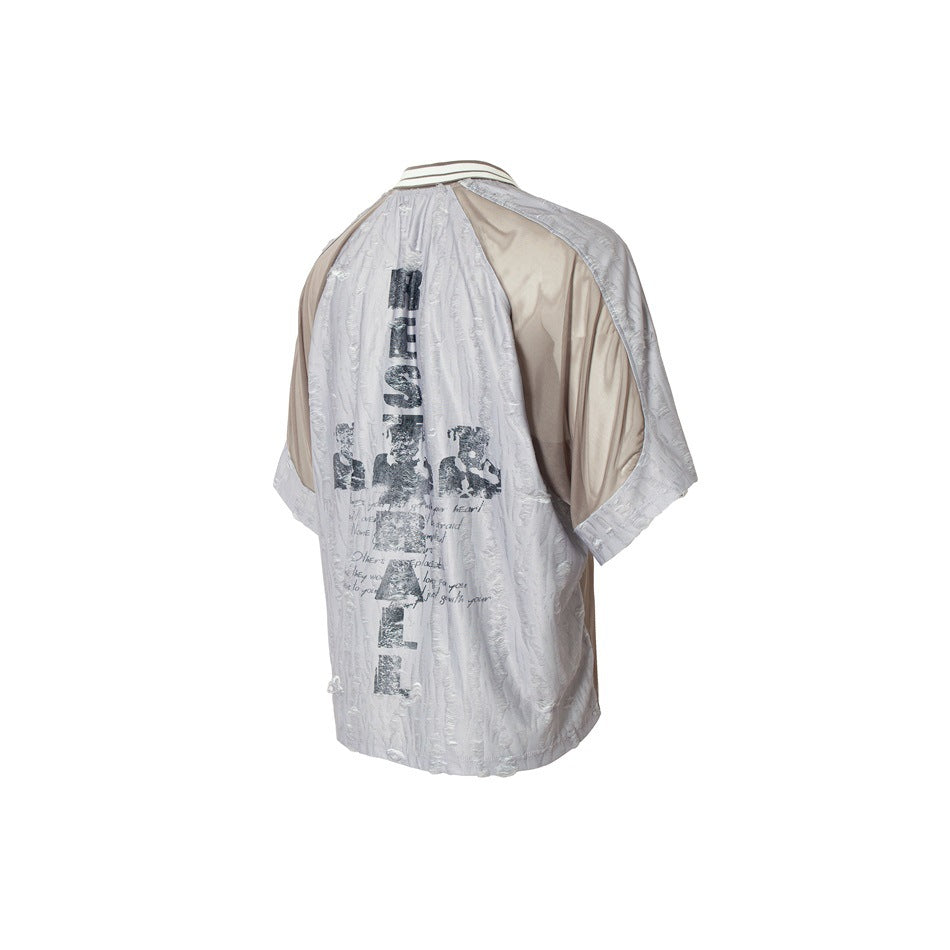 Angled back view of a pale gray textured shirt with taupe panels and a large dark printed graphic.