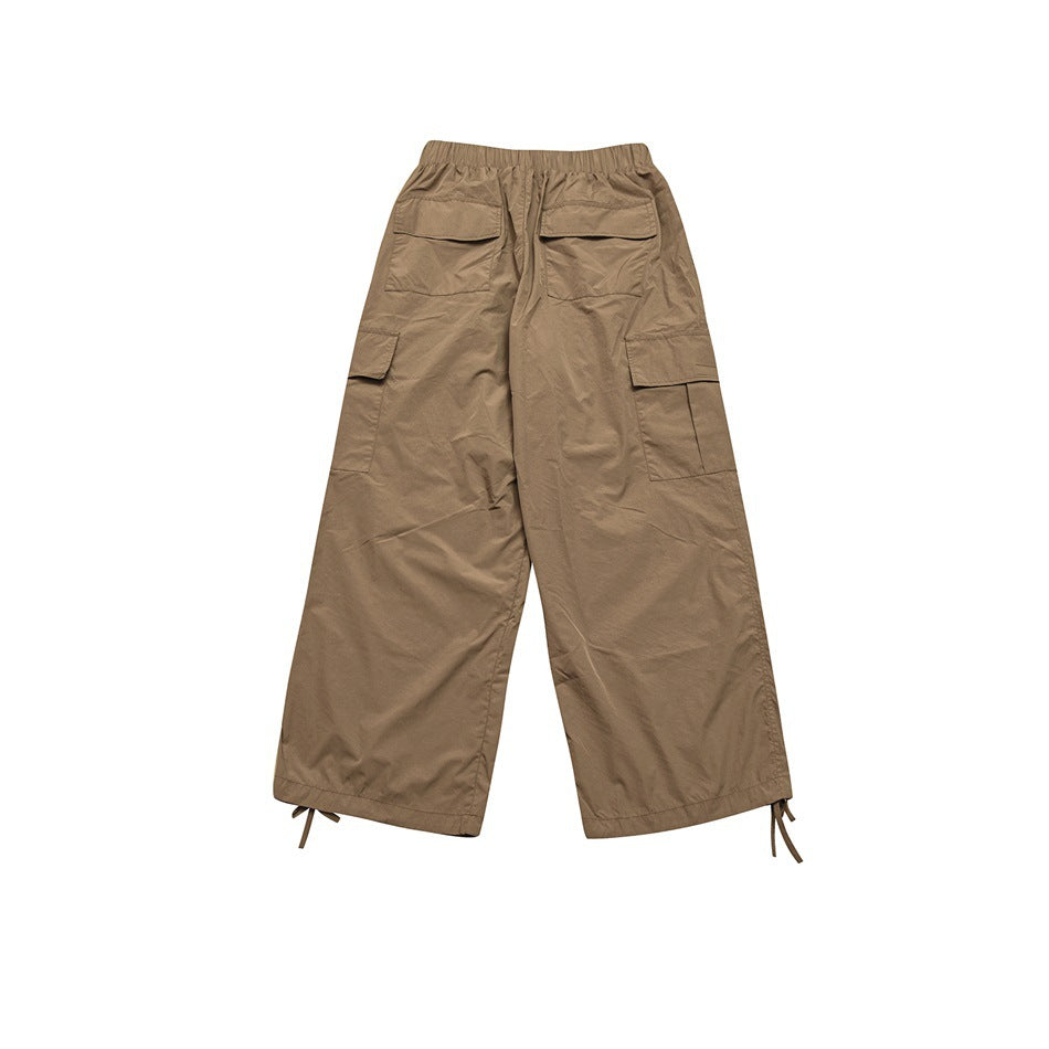 Back view of tan wide-leg cargo trousers with flap pockets, side cargo pockets and adjustable ankle ties.