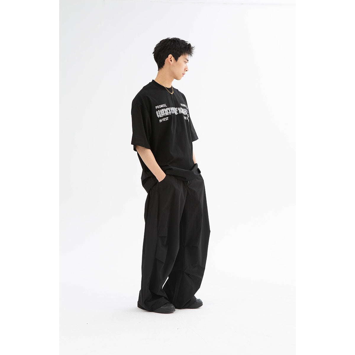 Side view of a model wearing an oversized black graphic T-shirt and very wide black trousers.
