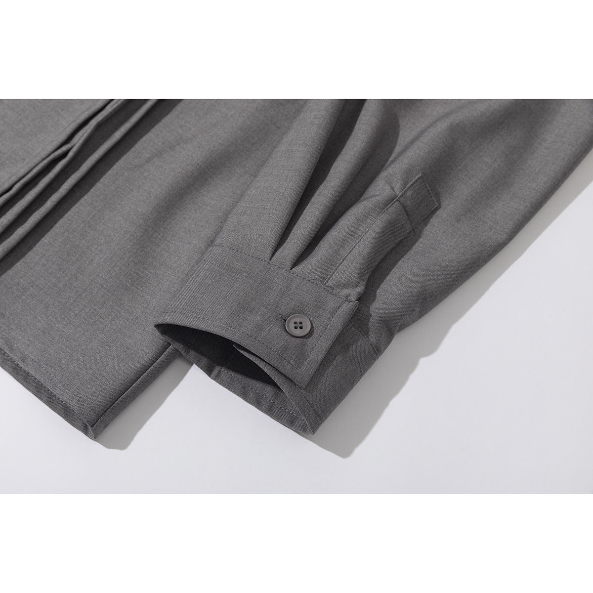 Close-up of a gray shirt sleeve cuff with a button and stitched pleat detail.