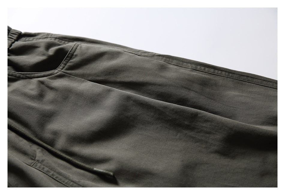 Partial flat lay of dark olive-gray pants showing the waistband, pocket opening, drawstring, and leg seam.