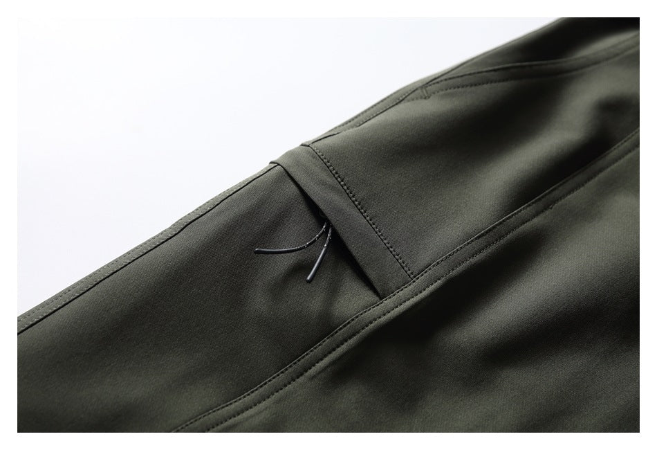 Close-up of dark olive pants with a narrow zip pocket and cord pull beside a seam.
