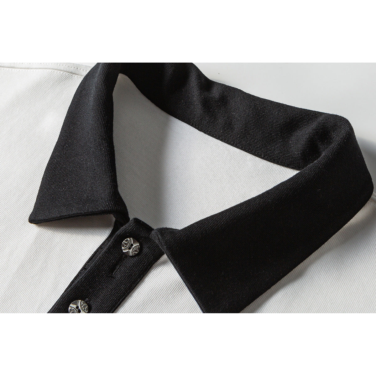 Close-up of a white polo shirt with a black collar and placket, featuring metallic buttons.