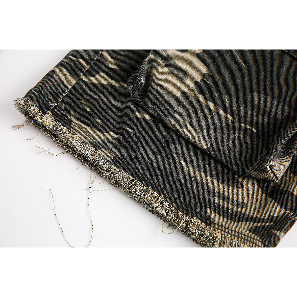 Close-up of the frayed raw hem on dark gray and tan camouflage shorts.