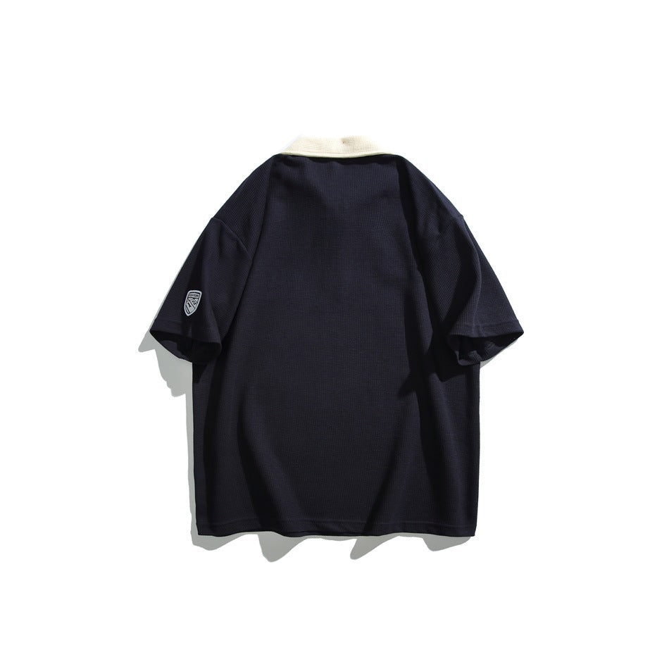 Navy waffle-knit short-sleeve polo back view with cream collar and shield patch on the sleeve
