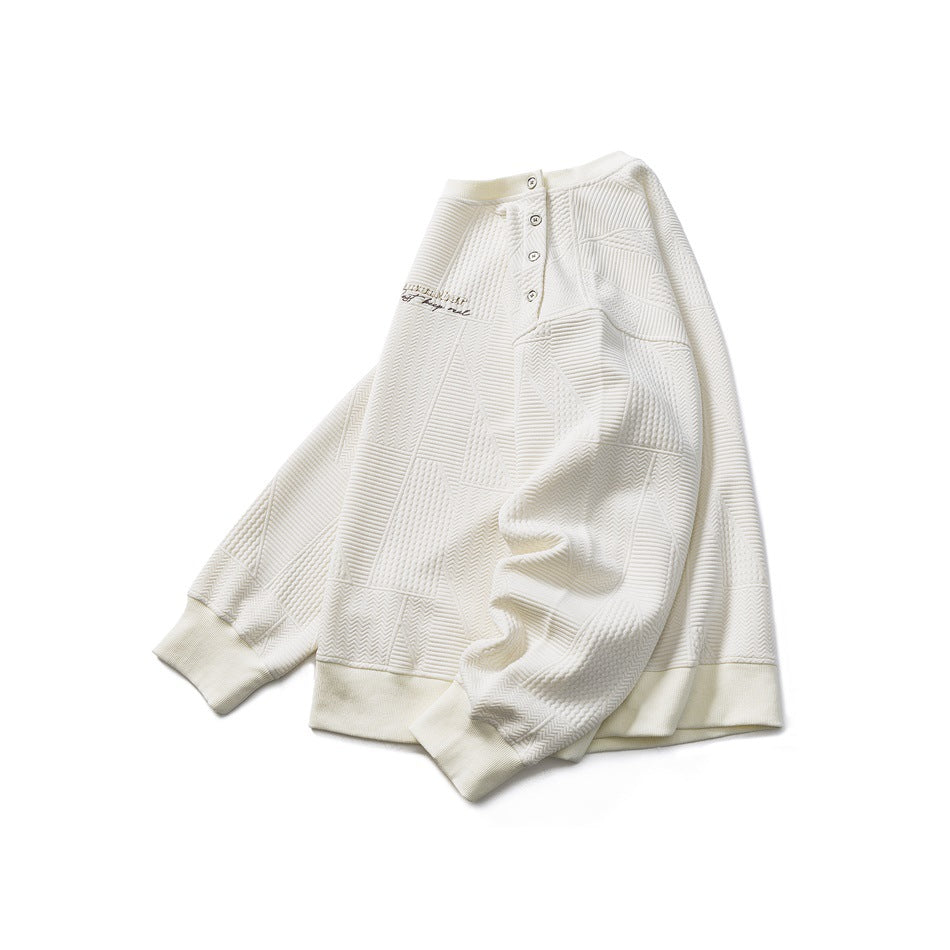 Ivory long-sleeve pullover laid flat, with a buttoned shoulder placket, geometric texture, and ribbed cuffs and hem.