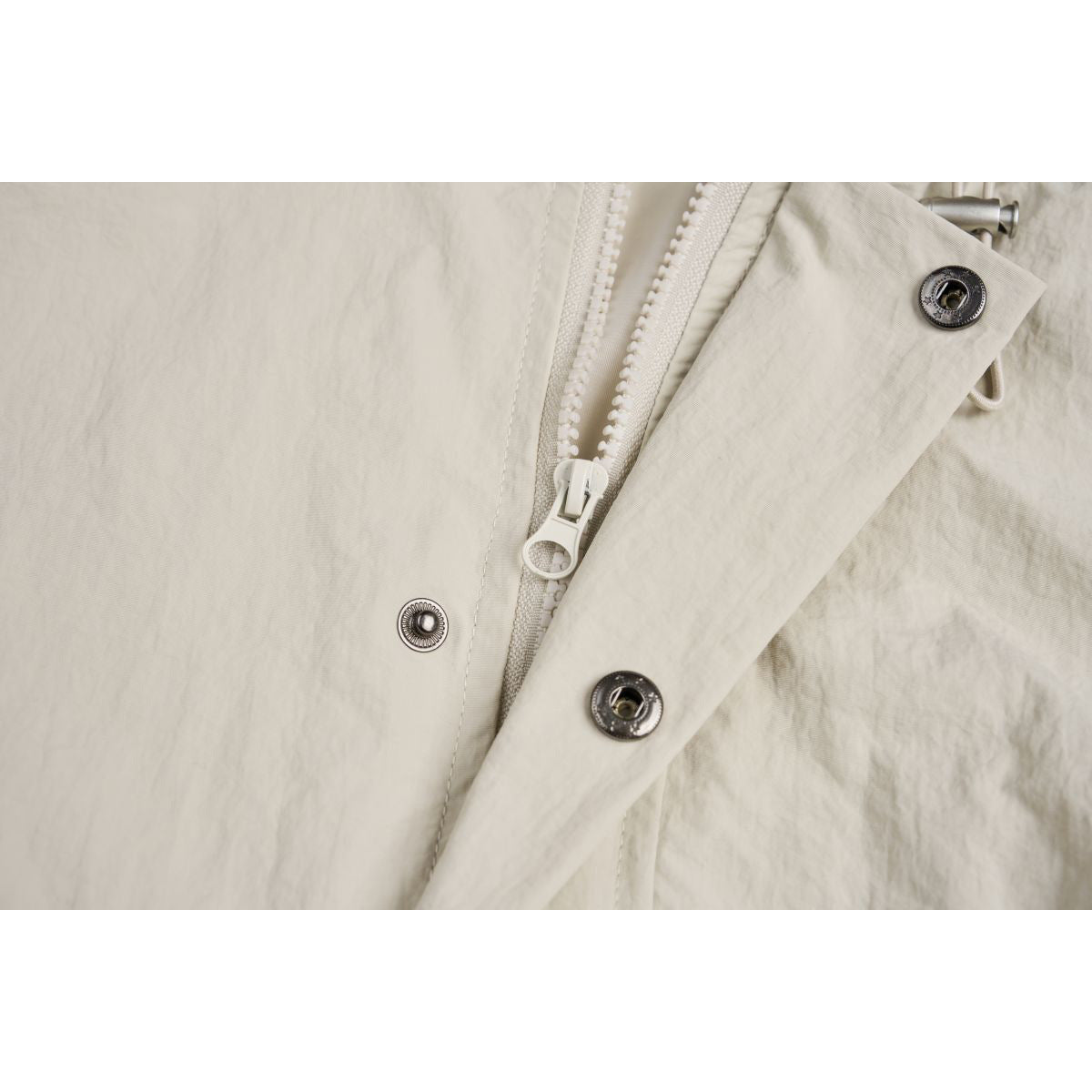 Close-up of the cream jacket's front zipper and metal snap fasteners.