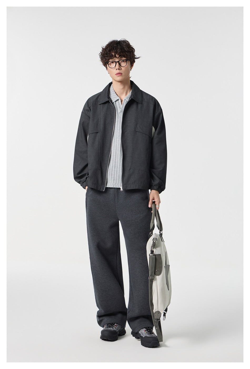 Full-length model wearing a charcoal zip-front jacket with a pointed collar and flap chest pockets, paired with dark pants.