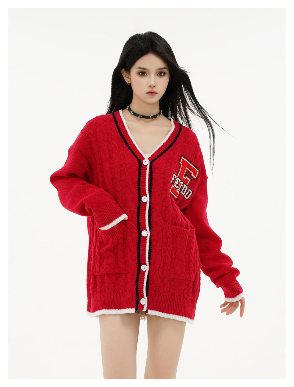 Model wearing a red cable-knit cardigan with striped trim, white buttons, two patch pockets and a letter patch.