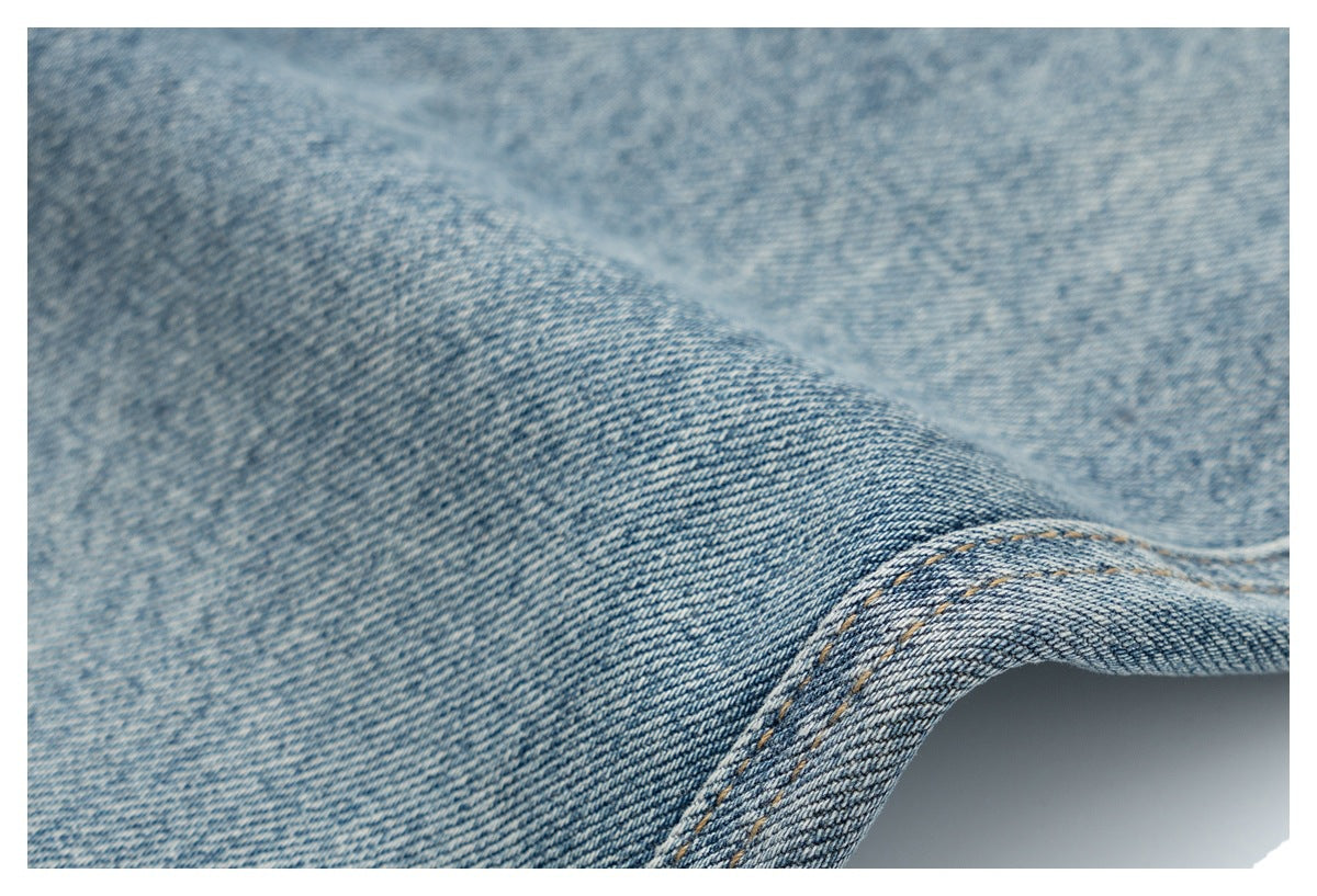Macro view of faded blue denim weave and a curved seam with tan stitching.