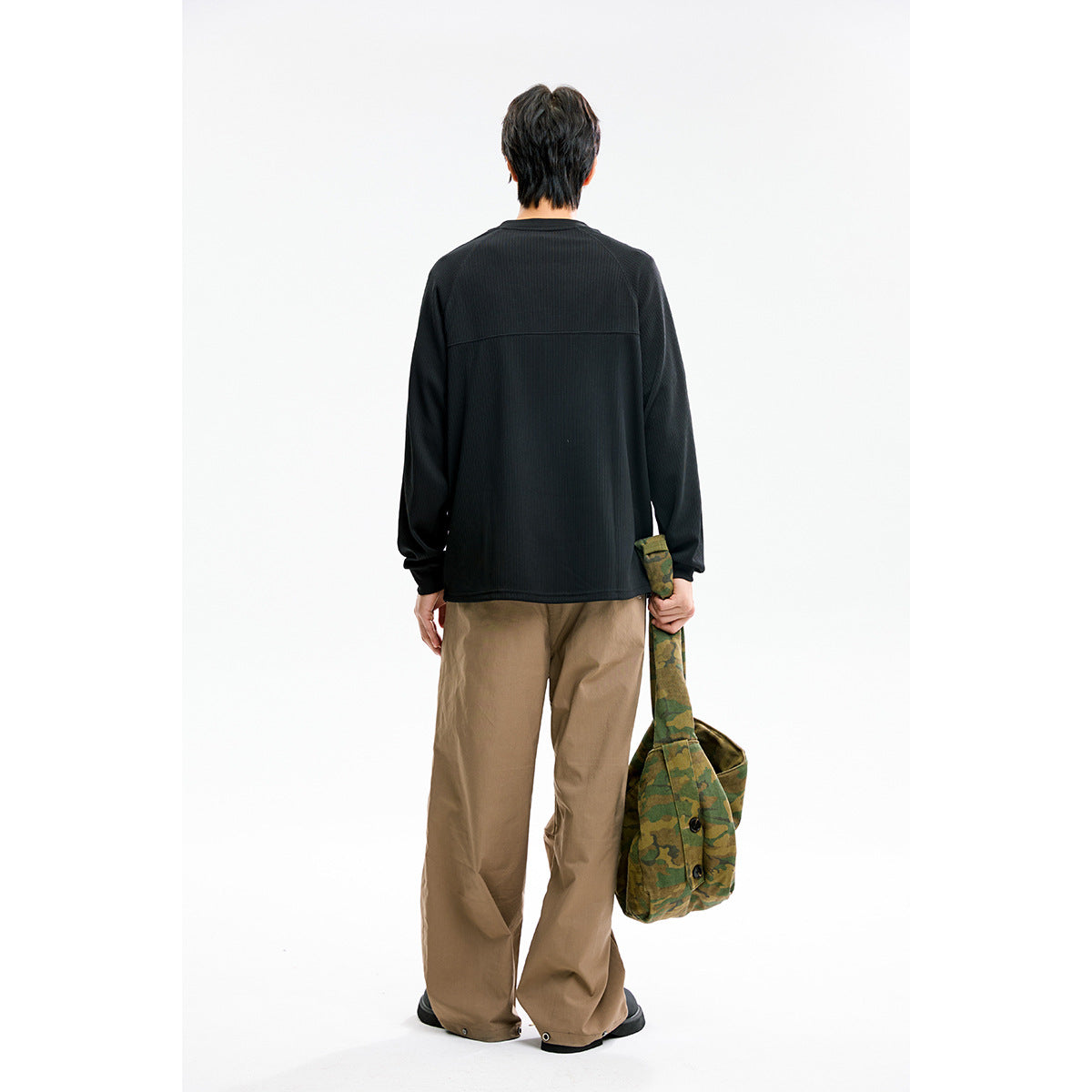 Rear view of a model wearing a black long-sleeve shirt and loose tan pants.