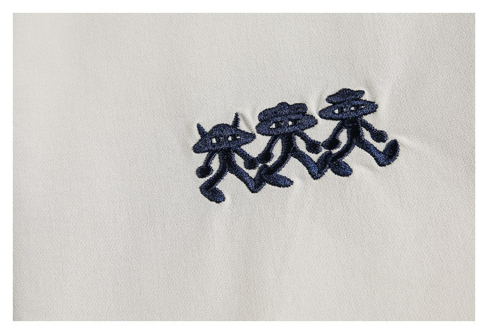 Close-up of three navy embroidered cartoon figures on beige fabric.