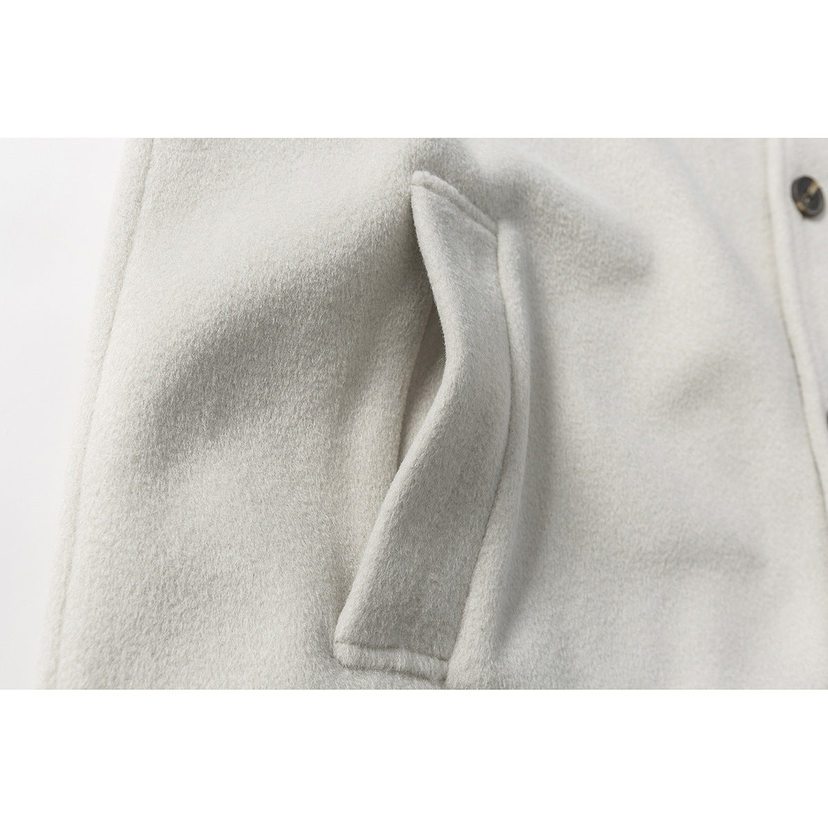 Close-up of a slanted welt pocket on an ivory coat beside its buttoned front.