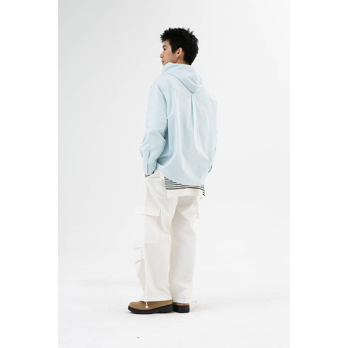 Rear view of a model wearing a pale blue hooded button-front shirt with white cargo pants.