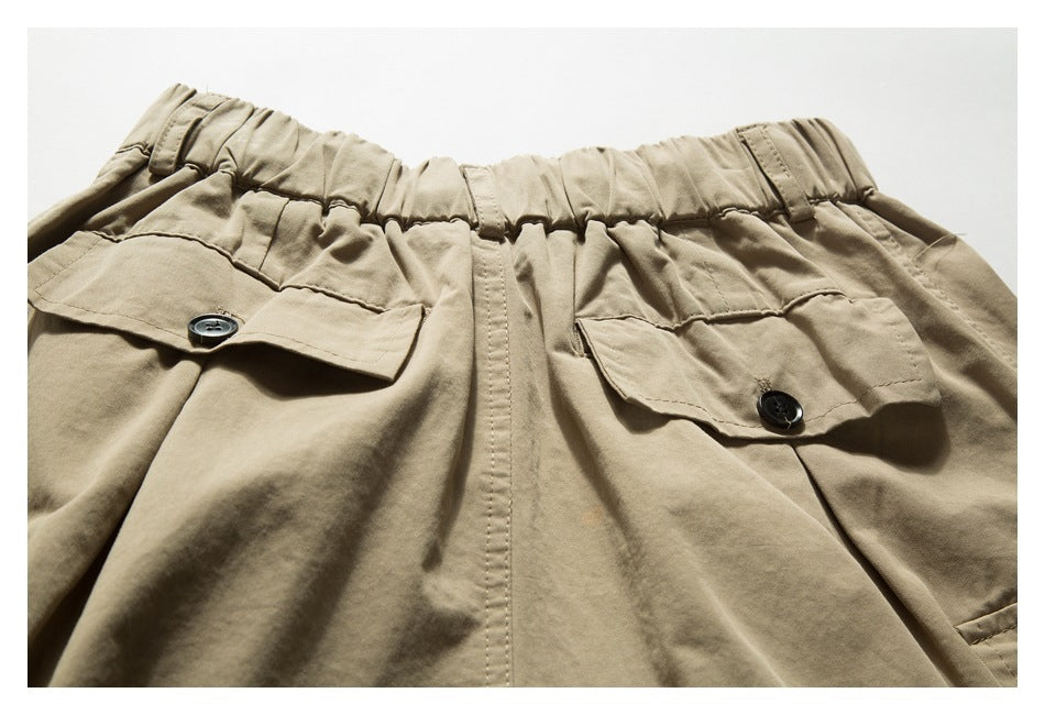 Close-up of tan trousers showing an elastic waistband and two buttoned flap pockets.