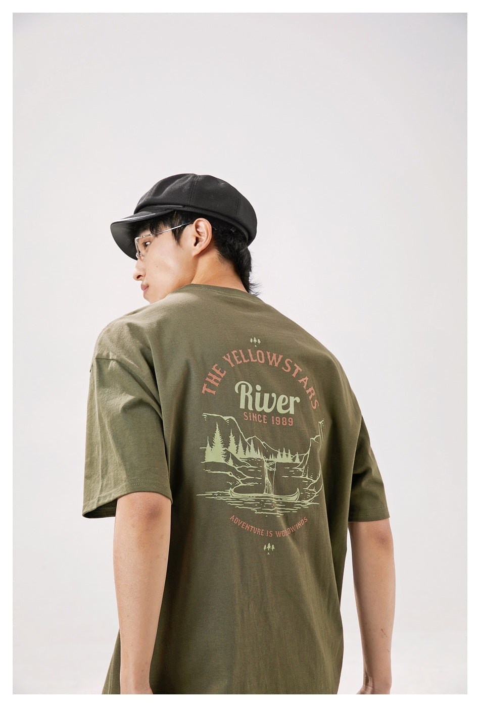 Model seen from behind wearing an olive oversized T-shirt with a large illustrated English back print.