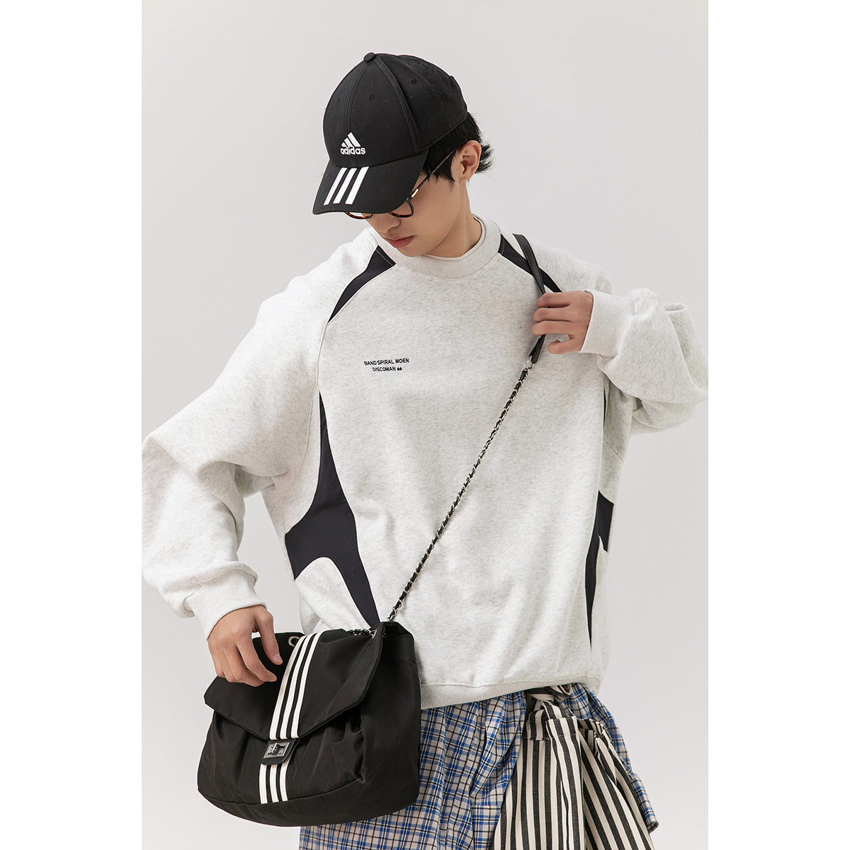 Model wearing a light gray sweatshirt with black curved panels, shown from the front.