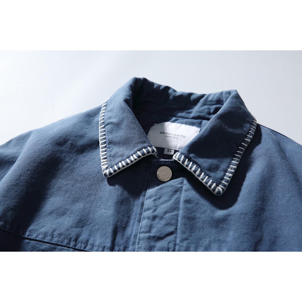 Close-up of a blue jacket collar with white contrast stitching, a metal button, and an inner size label.