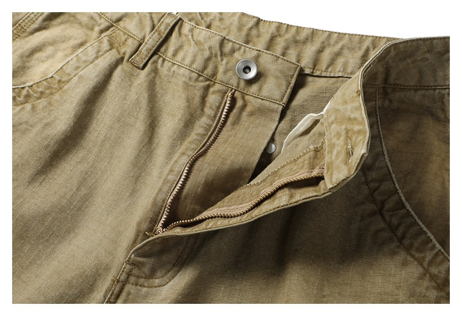 Close-up of tan pants with the waistband button and open zip fly.
