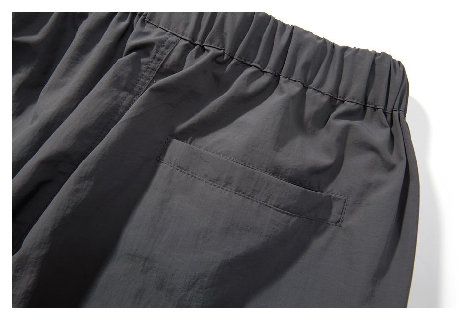 Close-up of dark charcoal pants with a gathered elastic waistband and rectangular rear pocket.