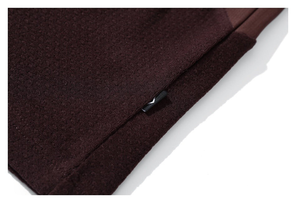 Close-up of a burgundy jacket hem with a small black tab and textured fabric.