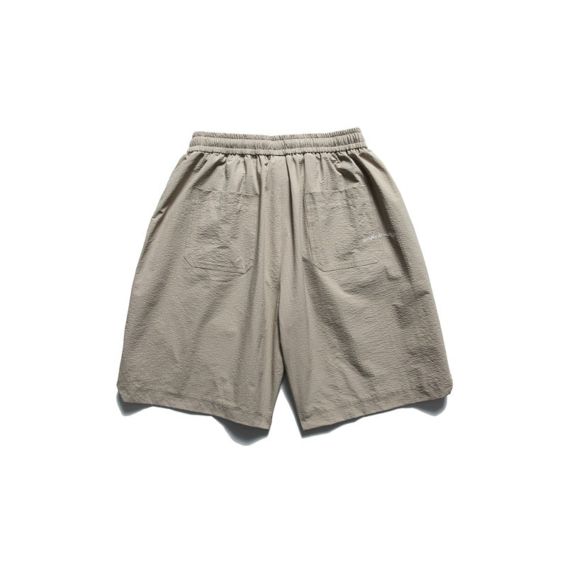 Back view of taupe shorts with an elastic waistband, two patch pockets and small white script near one pocket.
