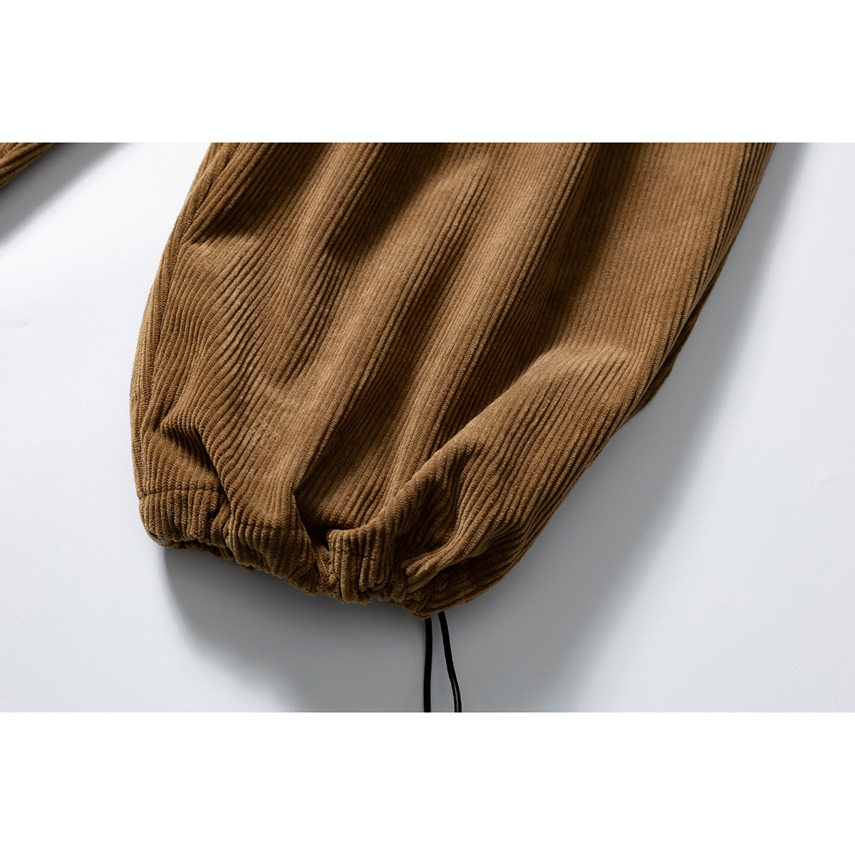 Close-up of a brown corduroy pant leg gathered at the cuff with a dangling black drawstring.